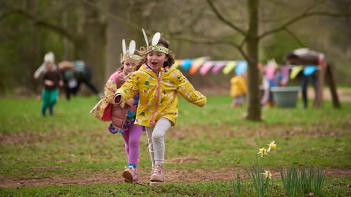 Two young girls wearing bunny ears run towards the camera laughing while enjoying an Easter trail